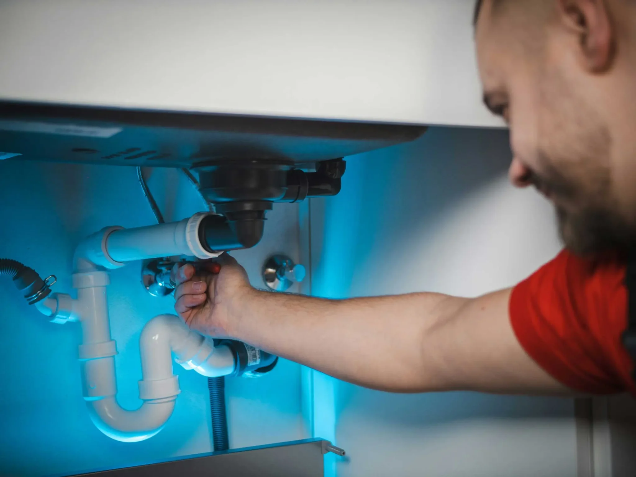 A plumber adjusting pipes under a sink with a wrench in a well-lit area.