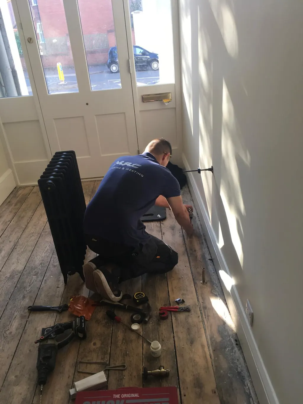 A plumber kneeling on the floor while working on a radiator installation in a room.