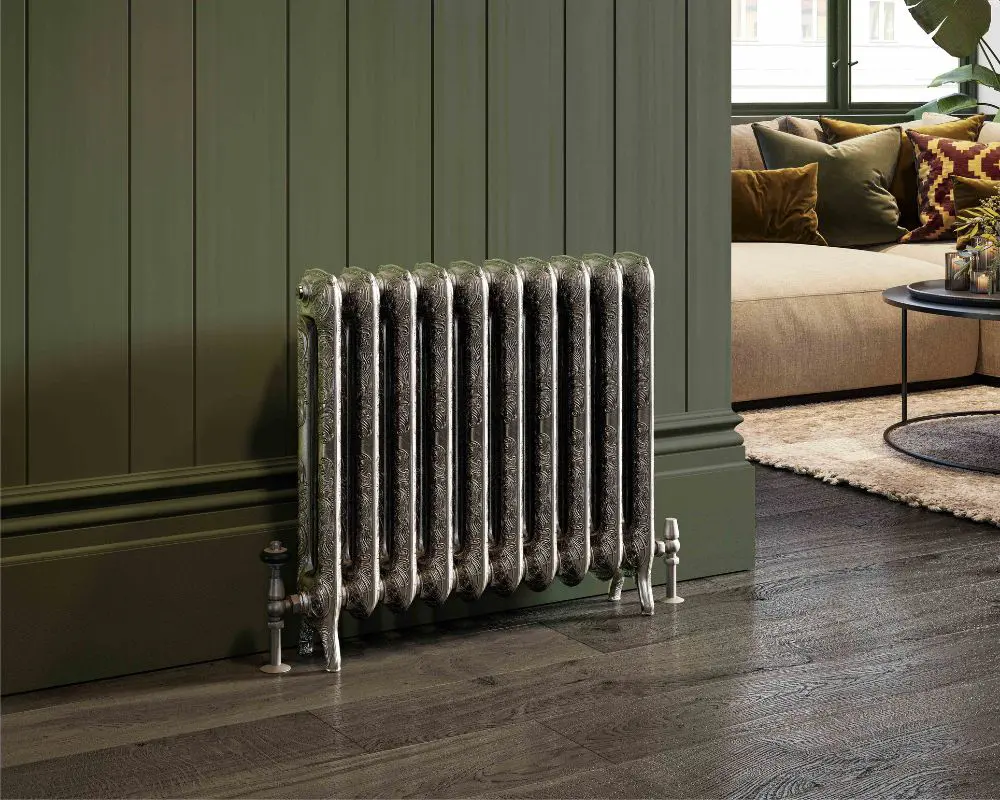A vintage-style radiator with a decorative design placed against a green wall.