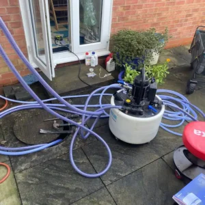 Plumbing equipment featuring a circular tank and multiple hoses, with potted plants nearby.
