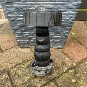 A black plumbing pipe connector with a spiral design and a flat top, placed on a textured surface.