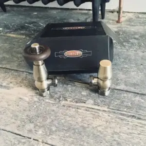 Two brass plumbing valves with wooden handles placed on a wooden surface next to a black box.