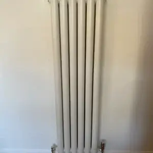 A vertical white radiator with multiple horizontal fins mounted on a wall.