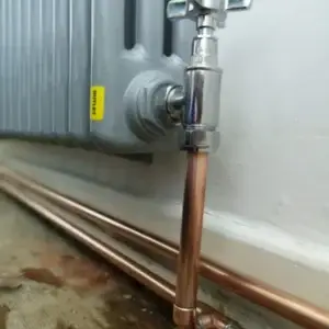 Copper pipe and valve connected to a radiator on a wall with visible plumbing.