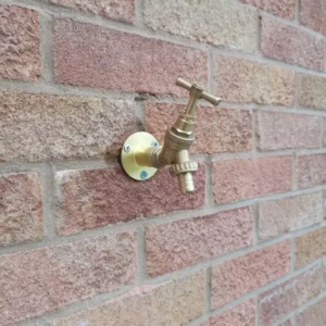 Brass garden tap with a handle mounted on a brick wall, featuring a round base and threaded outlet.