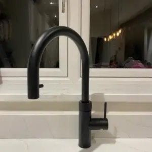 Black kitchen faucet with a curved spout and a lever handle installed by a window.