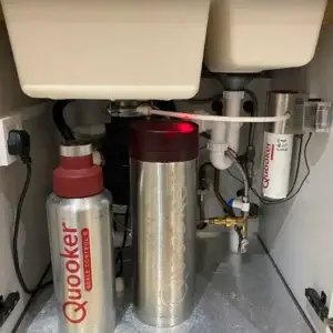 Quooker hot water tap system components including a tank and insulated bottle under a sink.