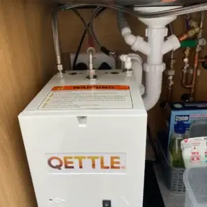 QETTLE instant hot water dispenser installed under a kitchen sink with warning label visible.
