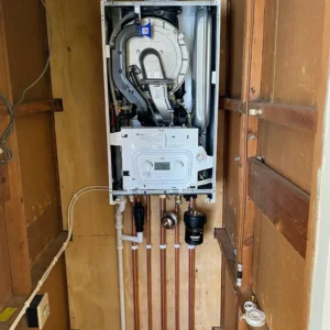 A wall-mounted boiler with connected pipes and components in a wooden enclosure.