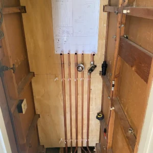Interior view of plumbing installation featuring copper pipes and a schematic diagram mounted on a wooden wall.