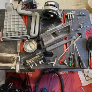 A collection of plumbing and heating tools arranged on a work surface, including wrenches, screws, and a vacuum attachment.